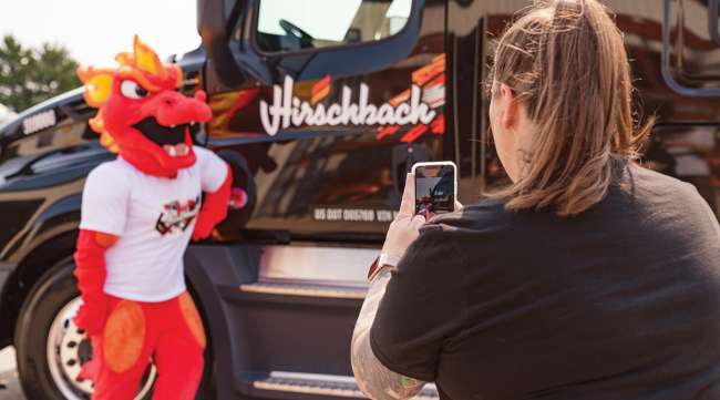 A woman snaps a photo of a mascot and a Hirschbach truck